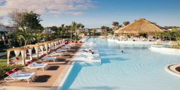 A pool with lounge chairs and a straw umbrella AI-generated content may be incorrect.
